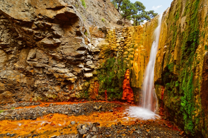 Cascada de Colores nella Caldera de Taburiente, con acqua ricca di minerali e tonalità arancioni sulla roccia vulcanica.